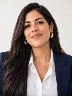 Woman with long dark hair and gold hoop earrings, wearing a navy blazer over a white shirt